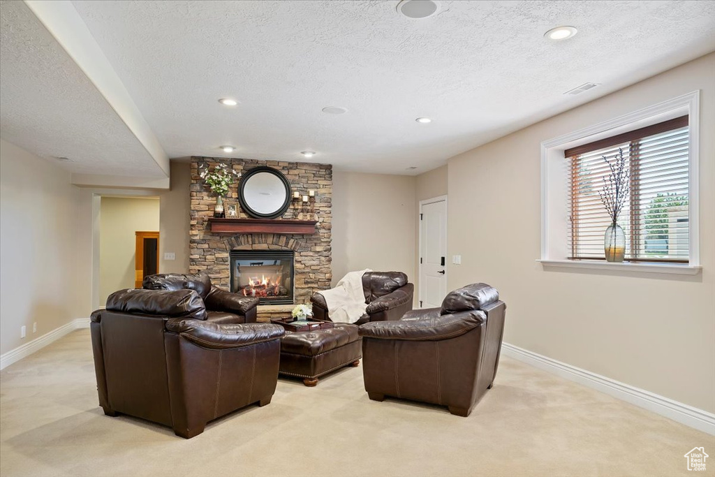 Living room with baseboards, a textured ceiling, a stone fireplace, and light colored carpet