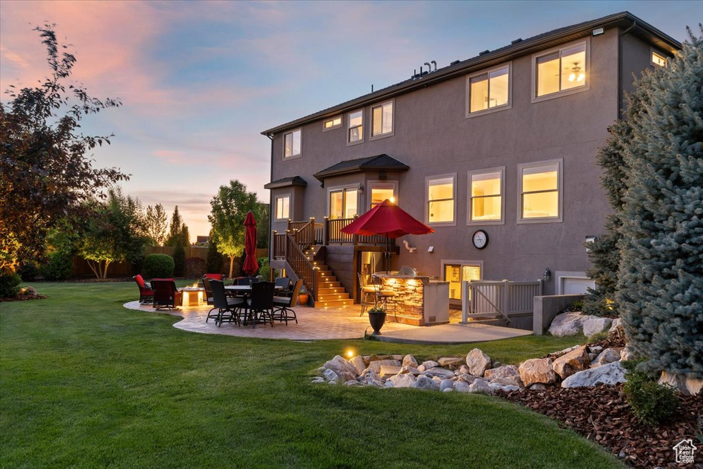 Back of house featuring stairs, stucco siding, a patio, and a yard