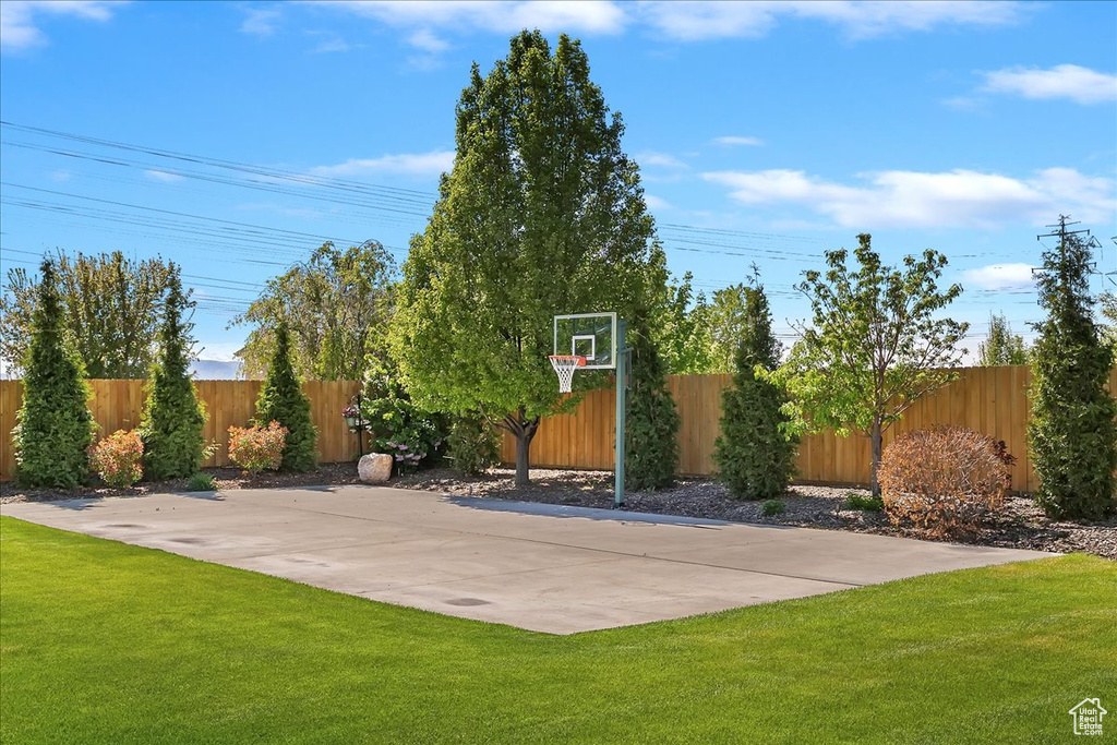 View of basketball court featuring a lawn, fence, and basketball hoop