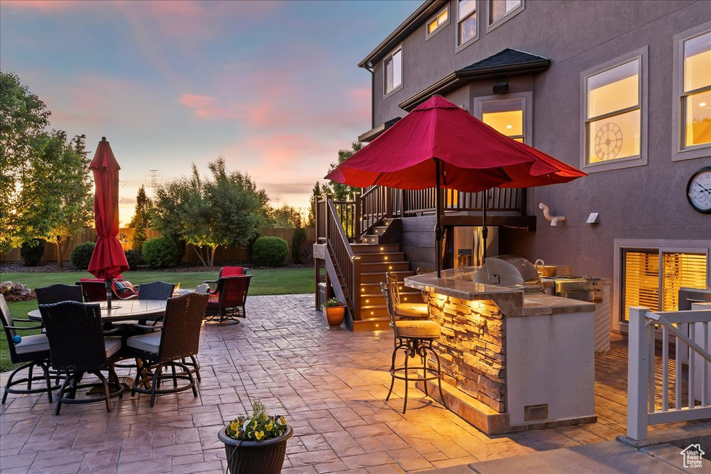 Patio terrace at dusk featuring stairway, an outdoor kitchen, a bar, outdoor dining area, and grilling area
