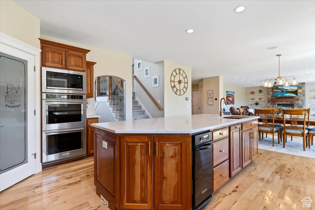 Kitchen with stainless steel double oven, light wood-style flooring, built in microwave, and a kitchen island with sink