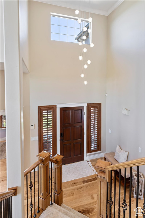 Foyer entrance featuring crown molding, an inviting chandelier, wood finished floors, and a towering ceiling