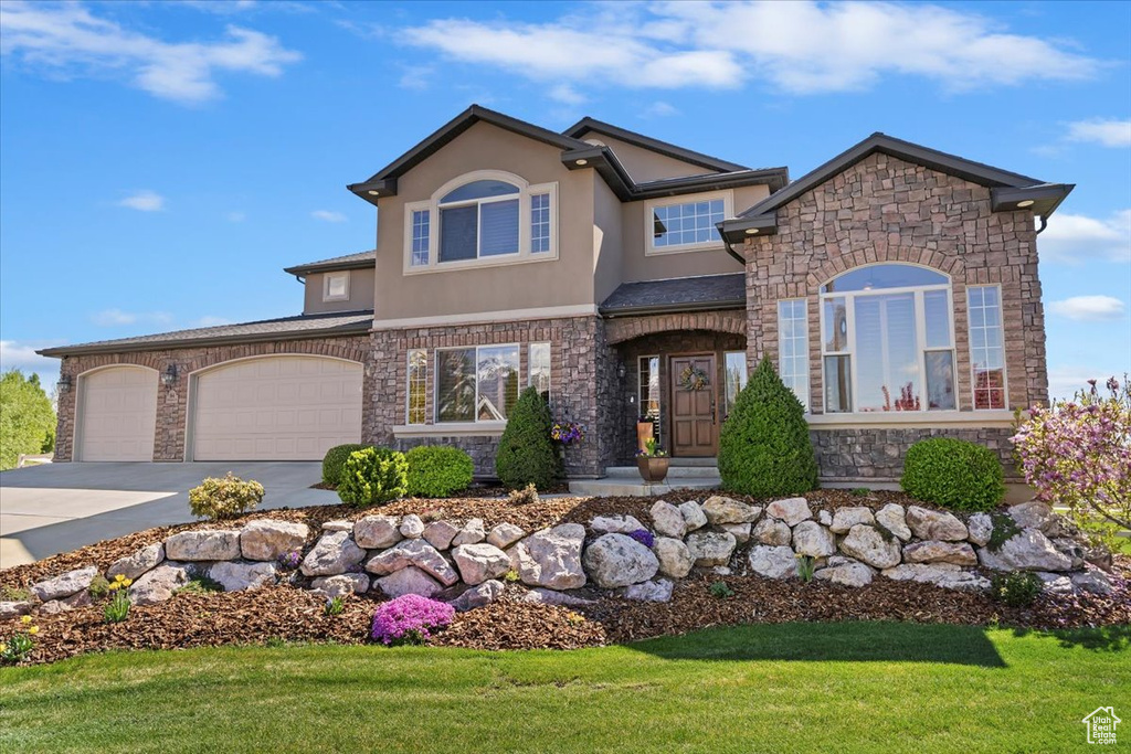 View of front of house featuring stucco siding, concrete driveway, a front lawn, and stone siding
