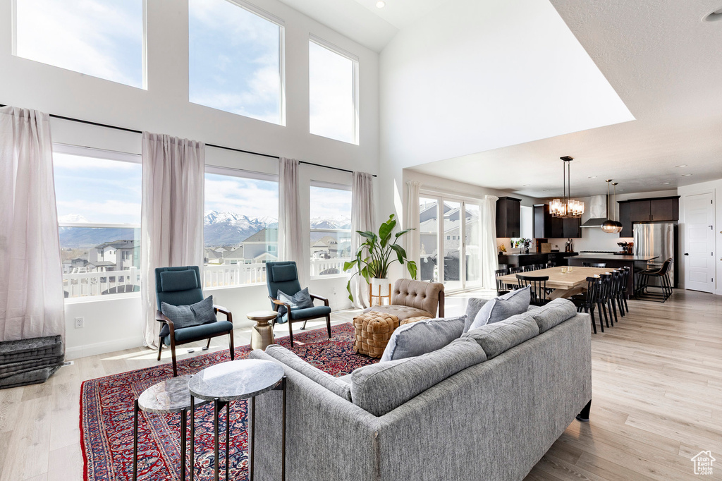 Living room with an inviting chandelier, a towering ceiling, light wood-style flooring, and a wealth of natural light