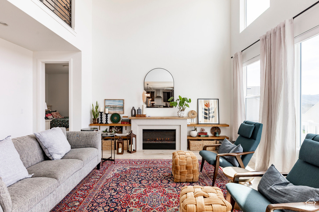 Living room with a towering ceiling, wood finished floors, and a lit fireplace