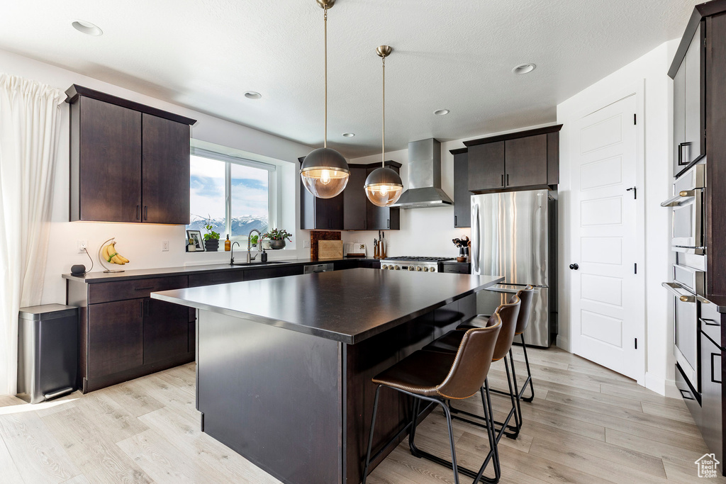 Kitchen featuring freestanding refrigerator, dark brown cabinets, a kitchen bar, wall chimney exhaust hood, and a sink