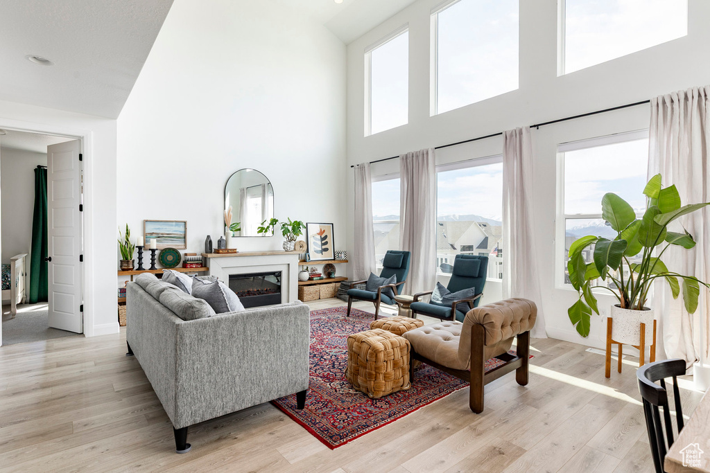 Living room featuring a glass covered fireplace, a high ceiling, and light wood-style flooring