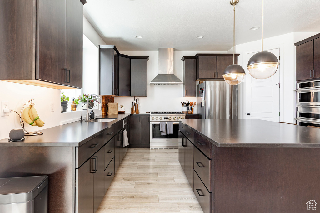Kitchen with dark countertops, appliances with stainless steel finishes, a kitchen island, and wall chimney range hood