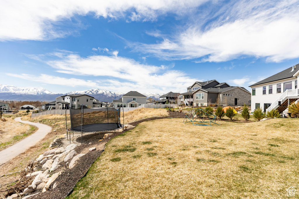 View of yard with a residential view, fence, a trampoline, and a mountain view