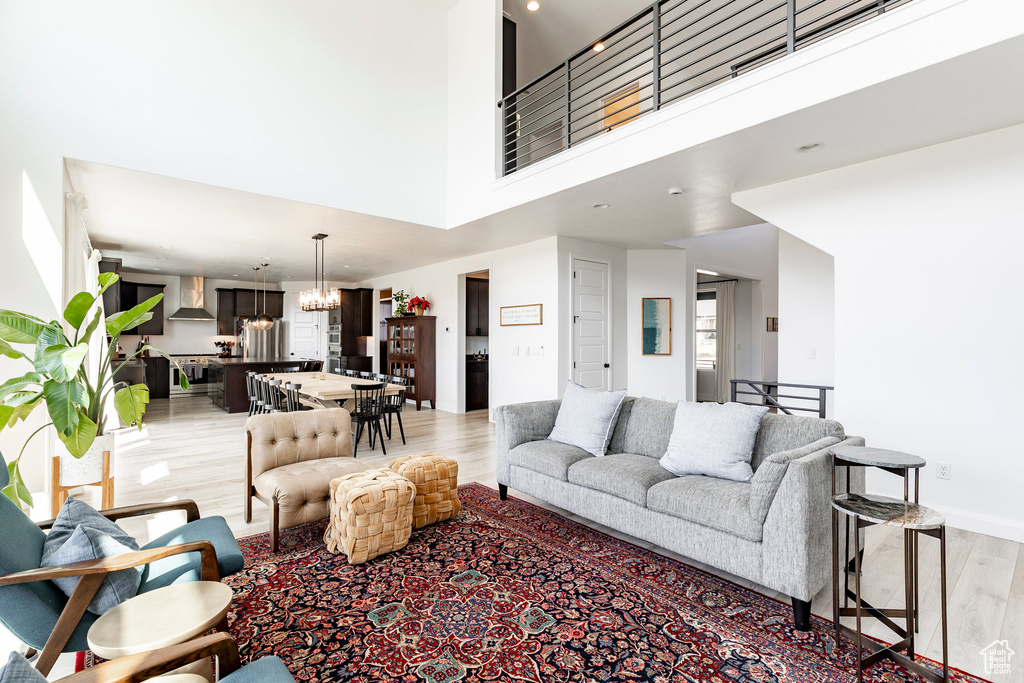 Living area featuring a towering ceiling, light wood-type flooring, baseboards, an inviting chandelier, and recessed lighting