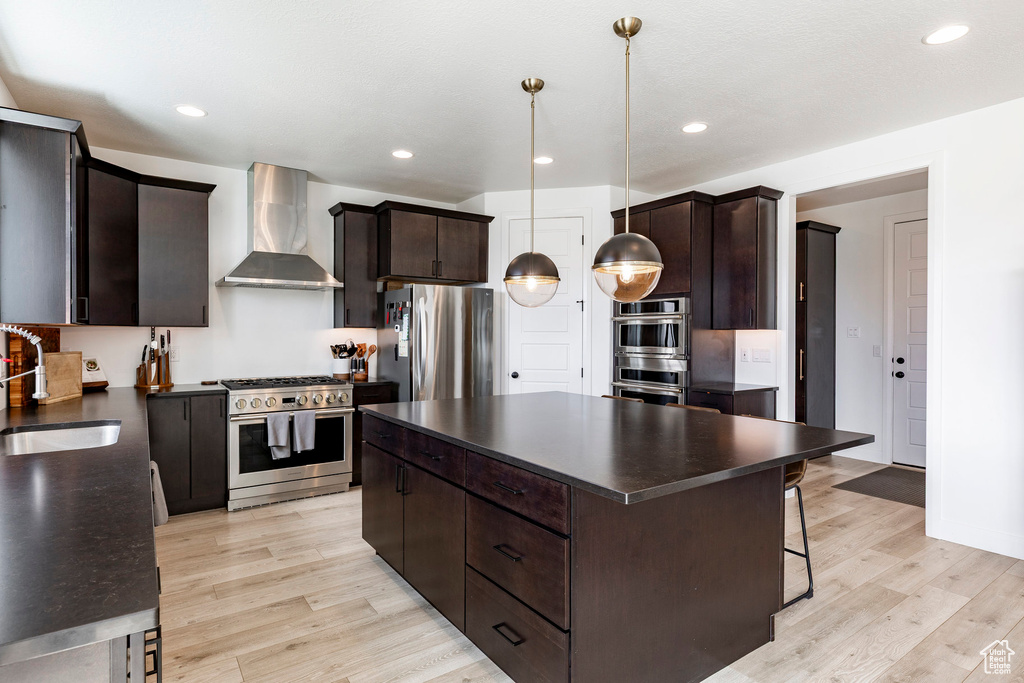 Kitchen featuring dark countertops, appliances with stainless steel finishes, a sink, light wood finished floors, and wall chimney exhaust hood