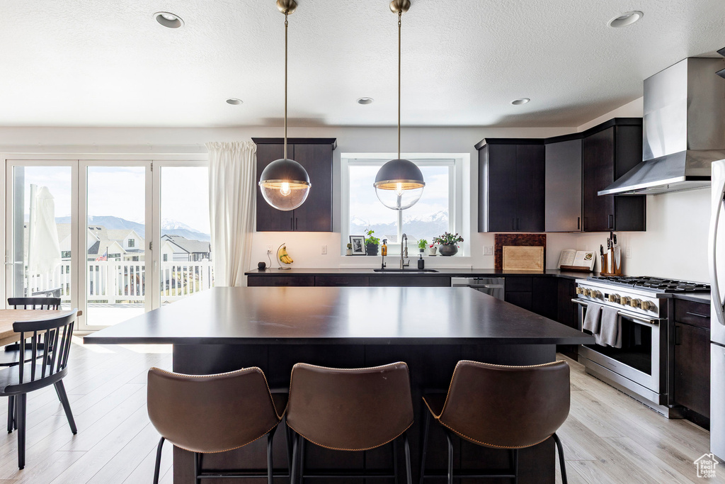Kitchen featuring a healthy amount of sunlight, dark countertops, a sink, stainless steel appliances, and wall chimney exhaust hood