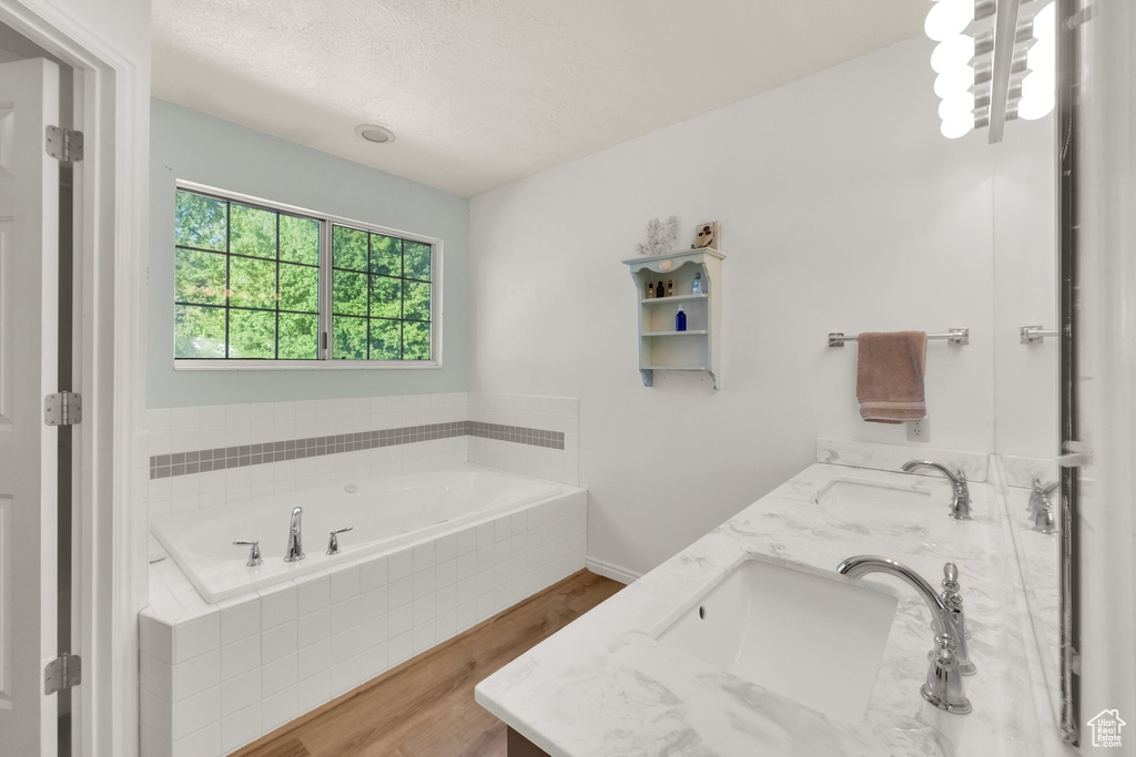 Bathroom featuring double vanity, a sink, wood finished floors, and a garden tub