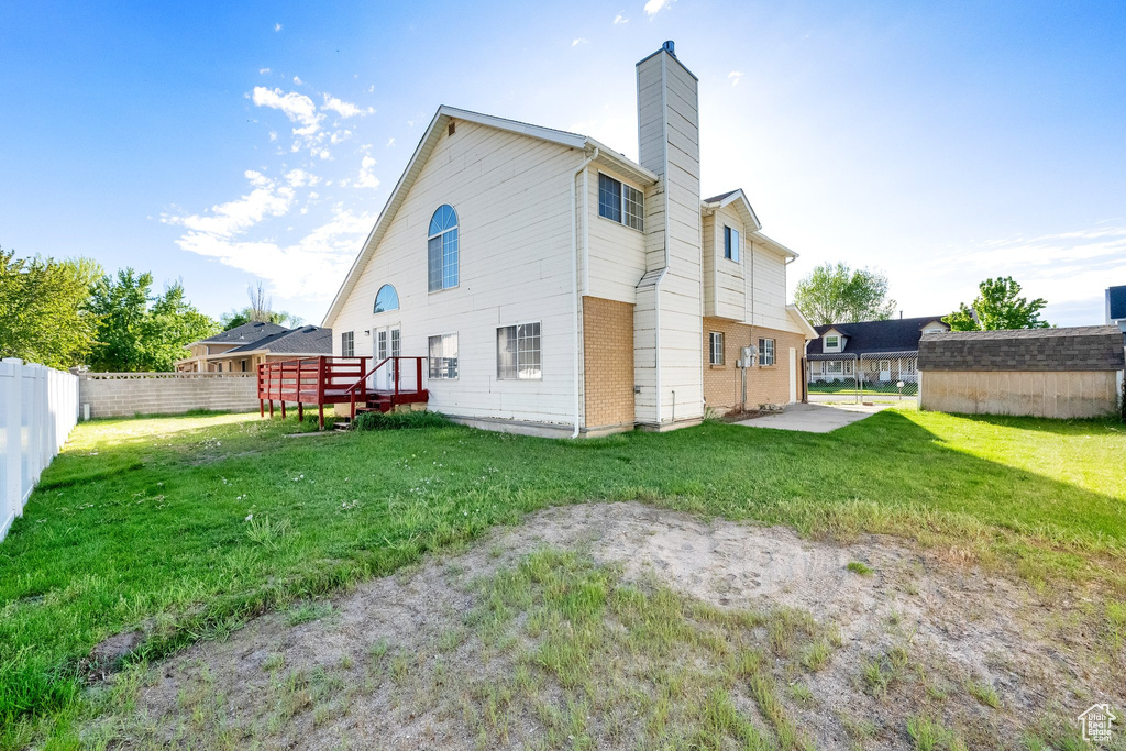 Rear view of property featuring fence, a deck, an outbuilding, a chimney, and a yard