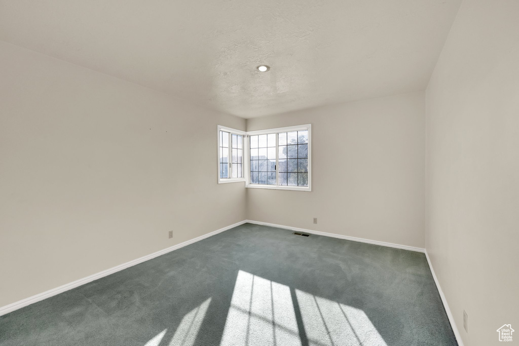 Unfurnished room featuring dark colored carpet, baseboards, and visible vents