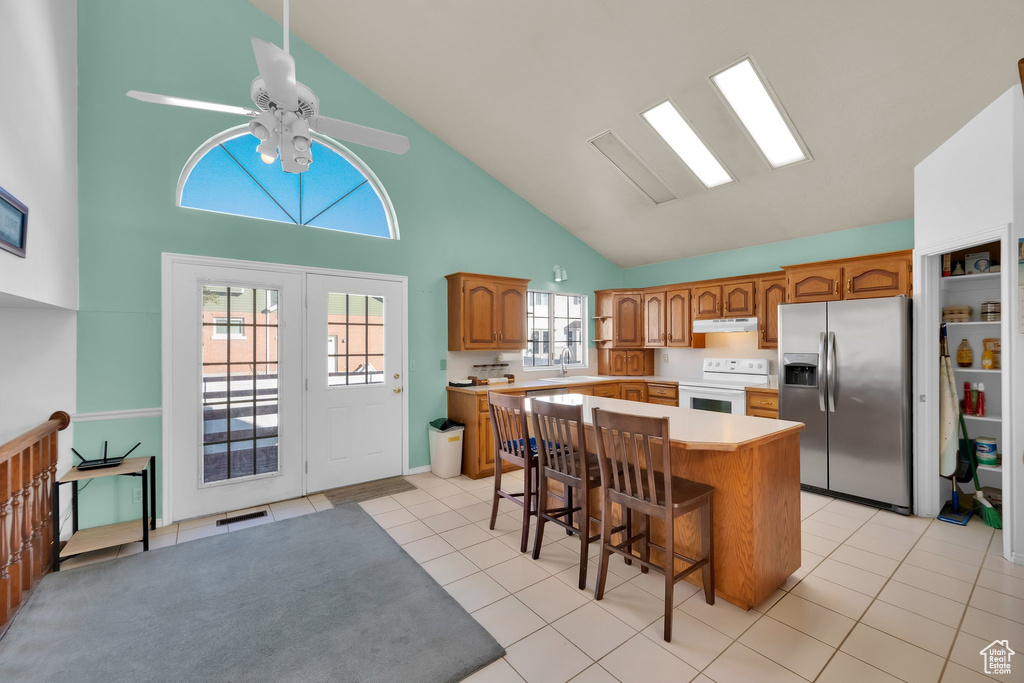 Kitchen featuring white electric range oven, stainless steel fridge with ice dispenser, high vaulted ceiling, brown cabinetry, and a kitchen island