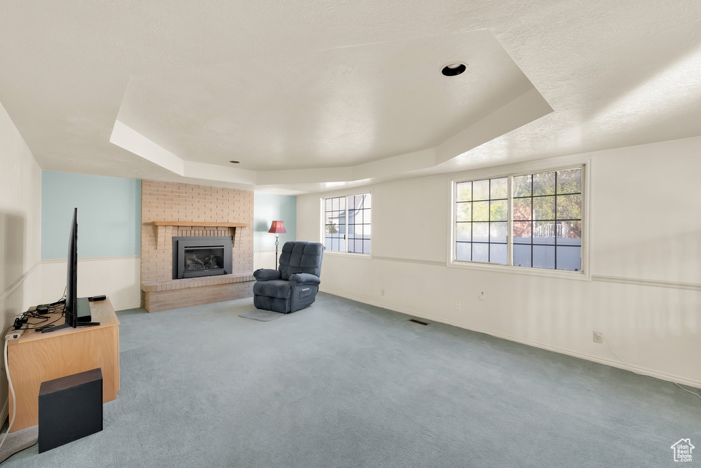 Unfurnished room featuring a brick fireplace, a tray ceiling, and carpet