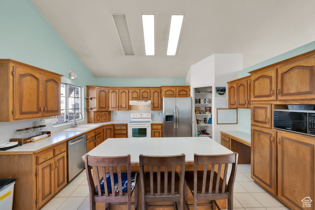 Kitchen featuring brown cabinetry, appliances with stainless steel finishes, light countertops, under cabinet range hood, and light tile patterned flooring
