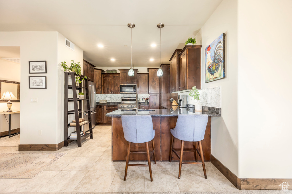 Kitchen with stainless steel appliances, dark brown cabinets, tasteful backsplash, a peninsula, and dark stone countertops