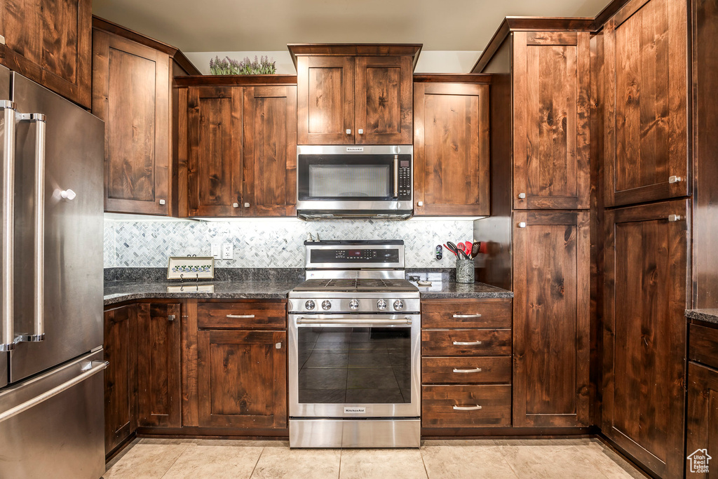 Kitchen with appliances with stainless steel finishes, decorative backsplash, dark stone counters, and light tile patterned floors