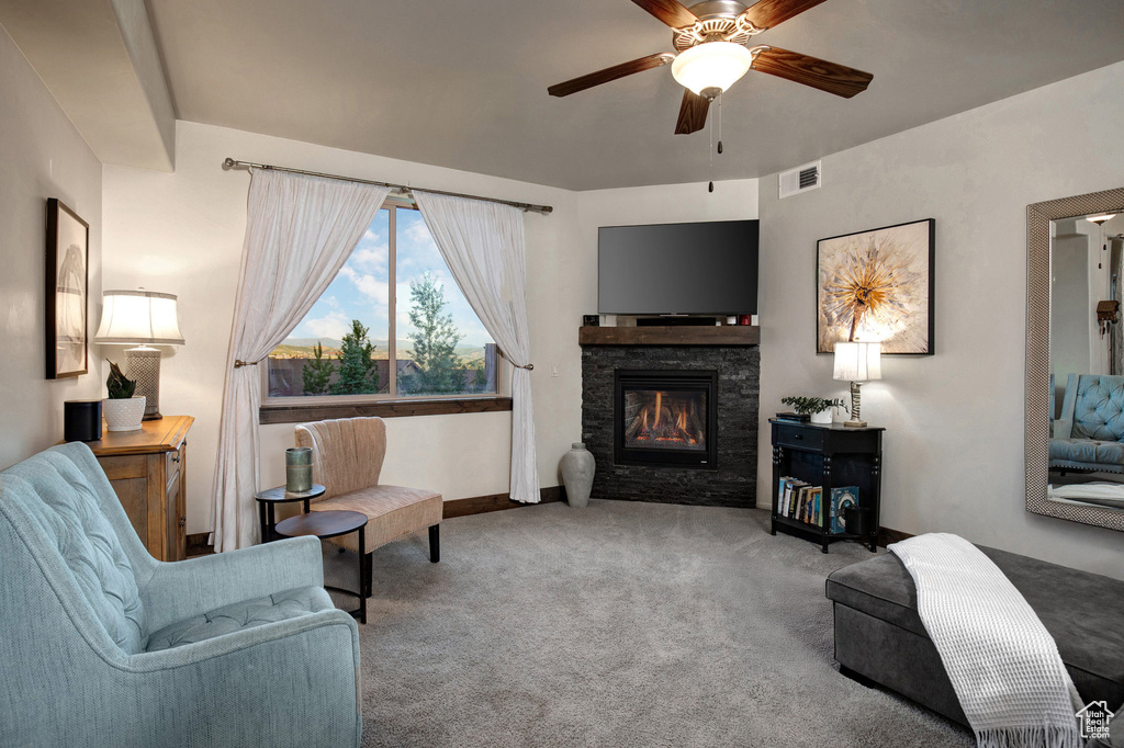 Carpeted living room featuring ceiling fan and a stone fireplace