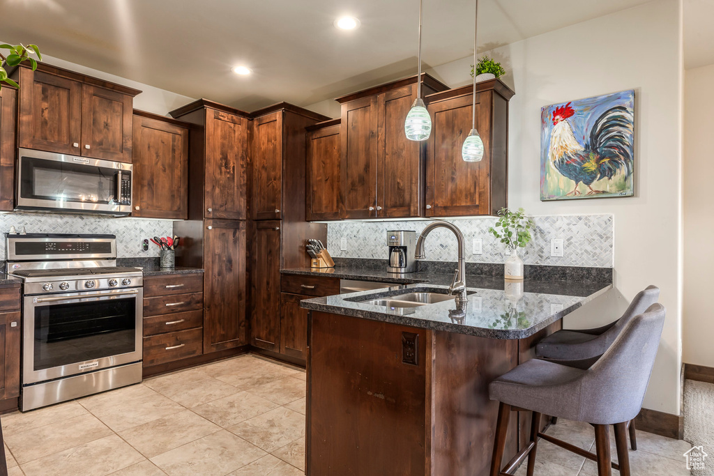 Kitchen with stainless steel appliances, backsplash, a peninsula, a breakfast bar area, and dark stone counters