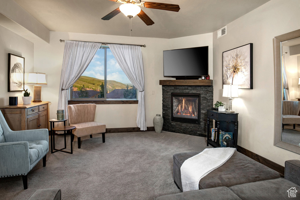 Carpeted living room featuring ceiling fan and a stone fireplace