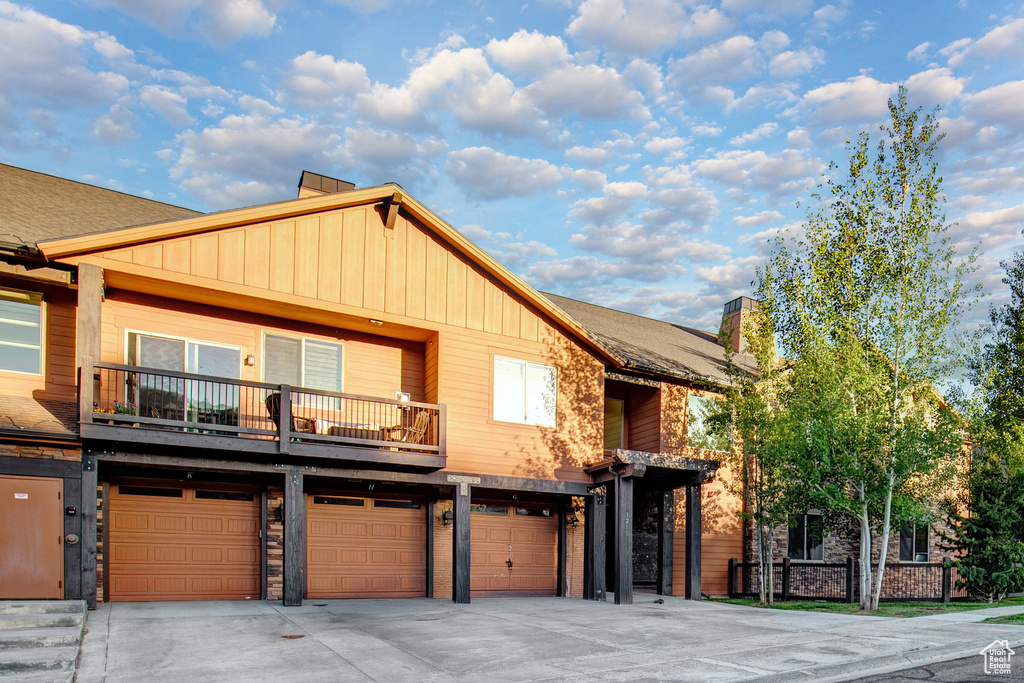 View of front of house featuring board and batten siding, an attached garage, a balcony, driveway, and a chimney
