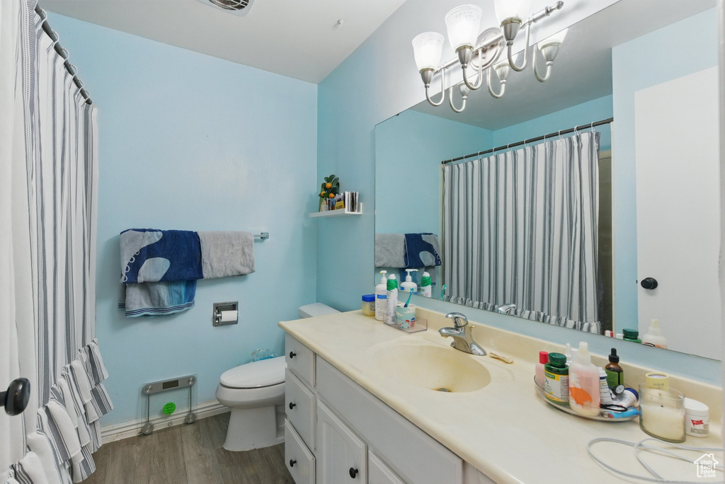 Bathroom with wood finished floors, vanity, baseboards, toilet, and a notable chandelier