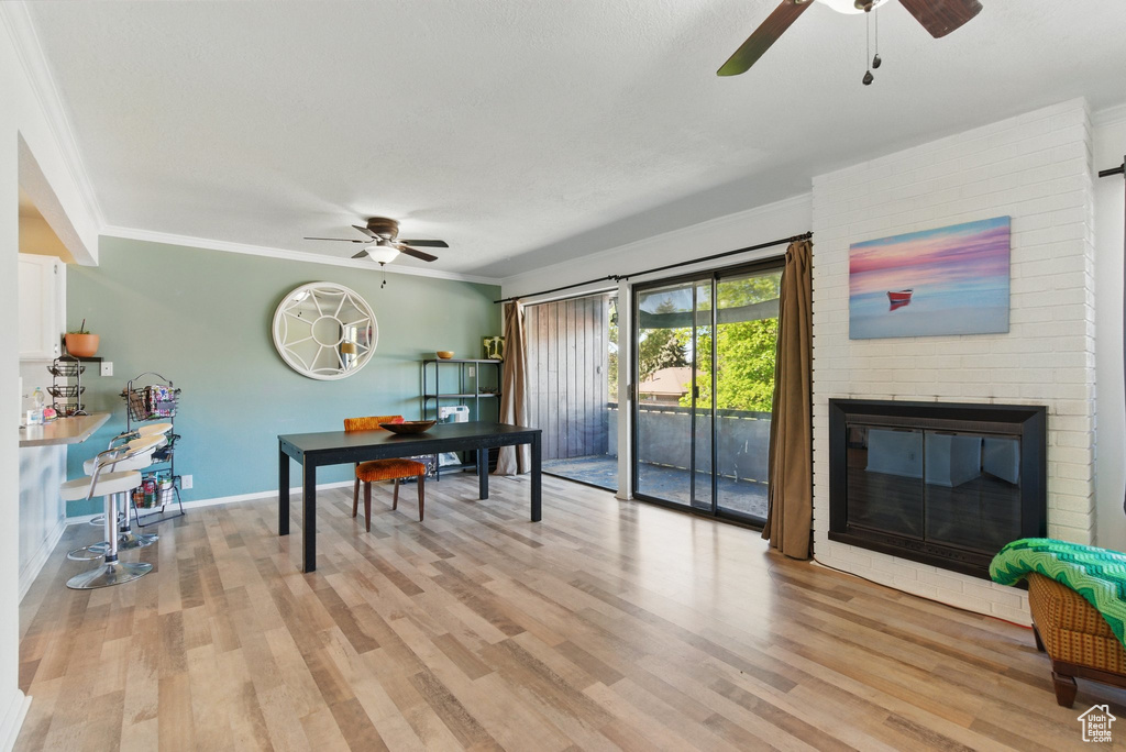 Home office with ceiling fan, ornamental molding, a brick fireplace, and light wood-type flooring