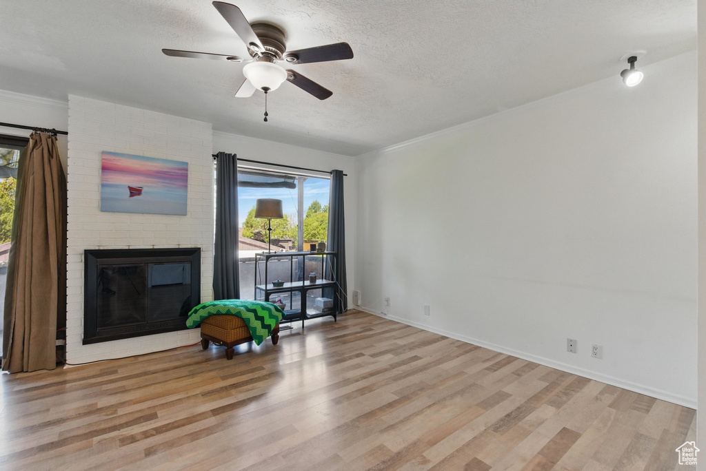Unfurnished living room featuring a brick fireplace, a ceiling fan, a textured ceiling, and wood finished floors