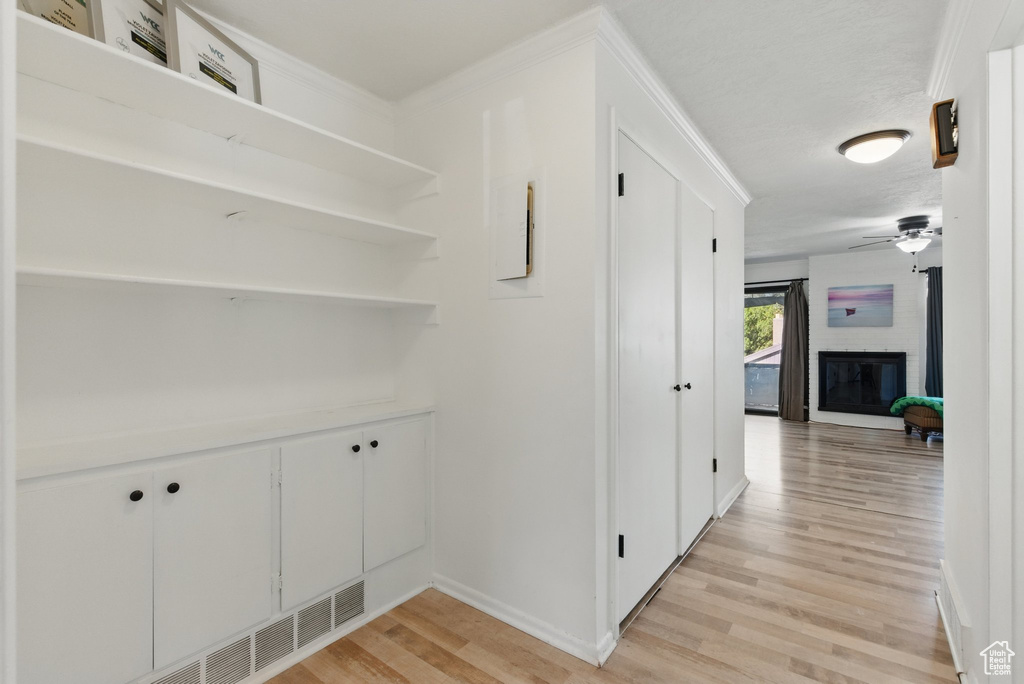 Hallway with light wood-style floors, baseboards, crown molding, and visible vents