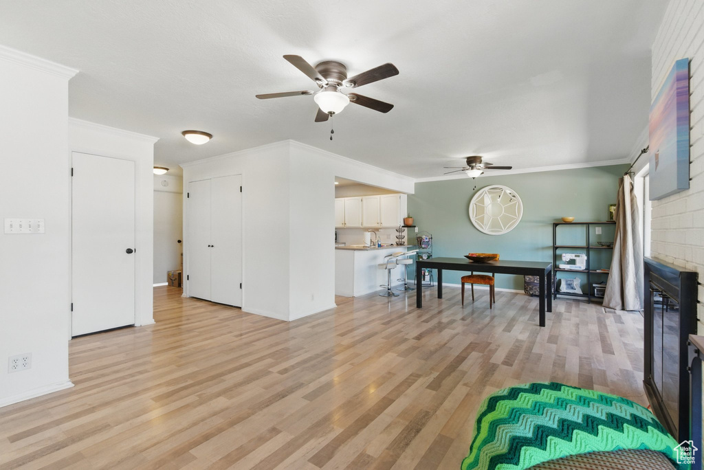 Living area with baseboards, ceiling fan, ornamental molding, and light wood-style flooring