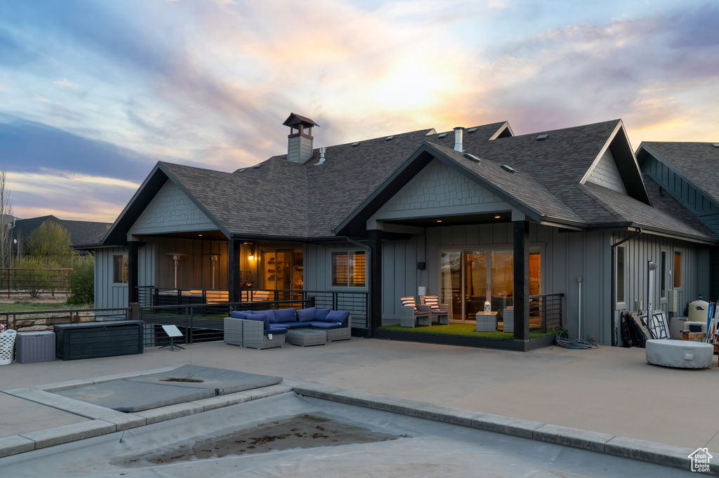 Back of property at dusk with a patio area, a chimney, board and batten siding, a shingled roof, and an outdoor hangout area