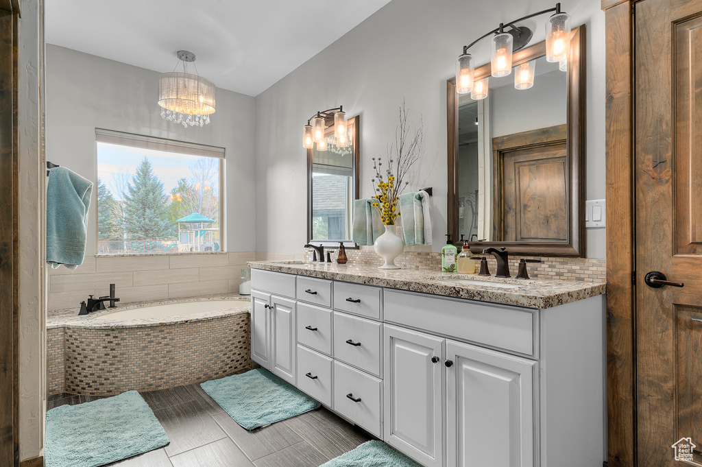 Bathroom with a chandelier, a bath, double vanity, and a sink