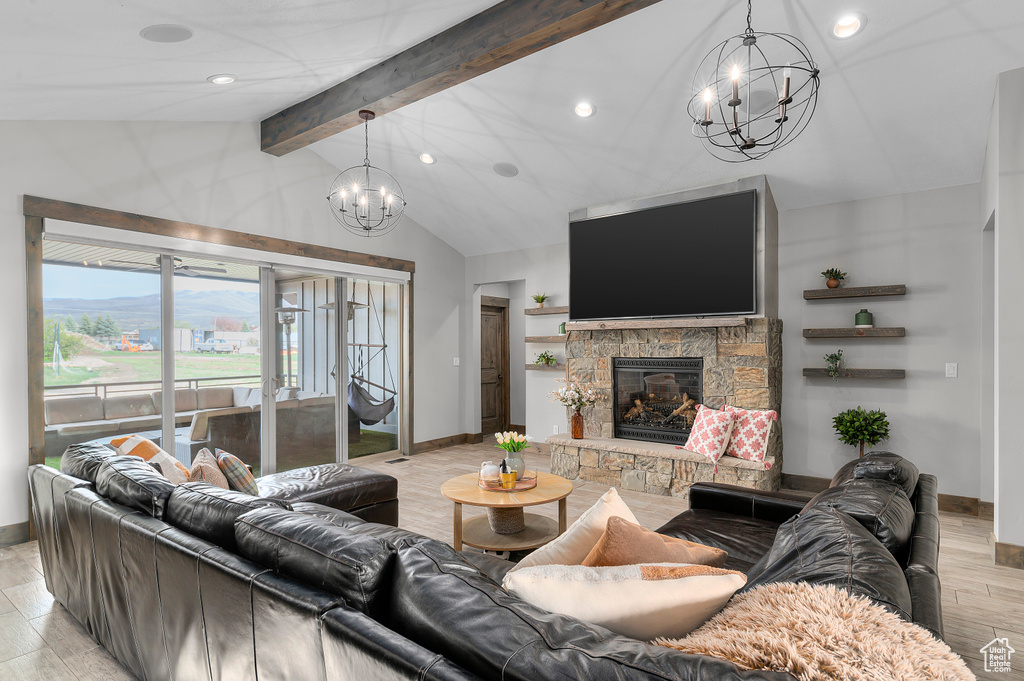 Living room featuring lofted ceiling with beams, baseboards, recessed lighting, a notable chandelier, and a stone fireplace