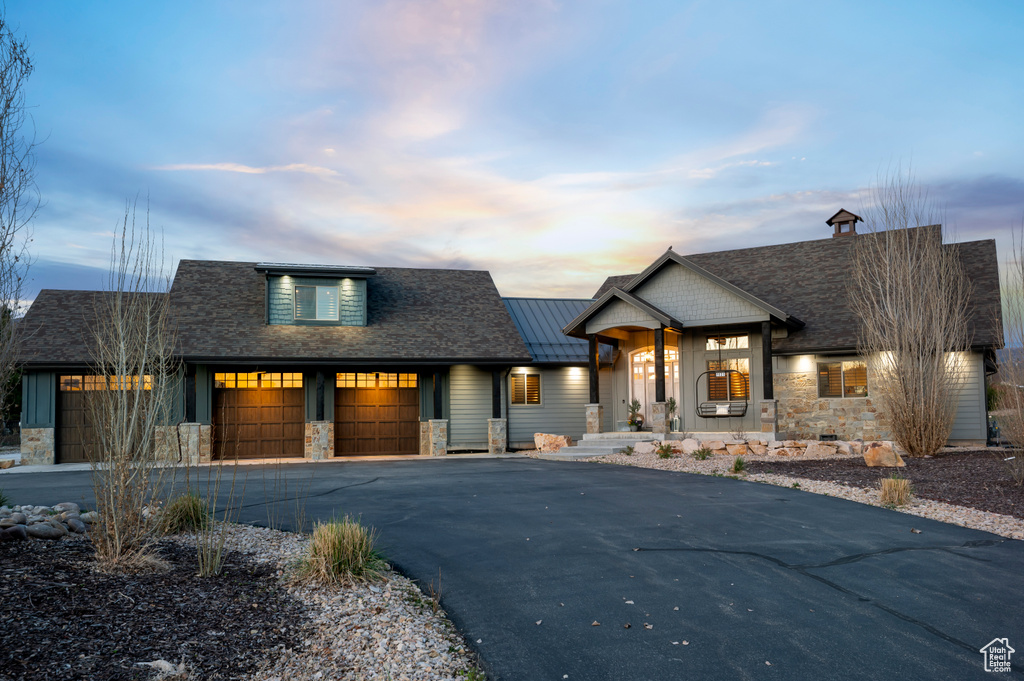 View of front facade featuring stone siding, an attached garage, driveway, and covered porch