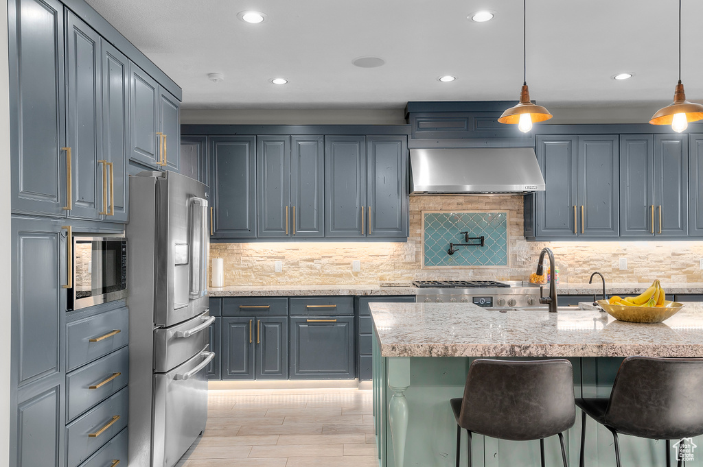 Kitchen featuring wall chimney exhaust hood, stainless steel appliances, a kitchen breakfast bar, recessed lighting, and light stone countertops