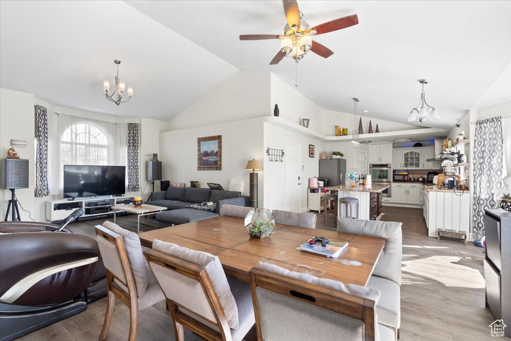 Dining area featuring ceiling fan with notable chandelier, wood finished floors, and lofted ceiling
