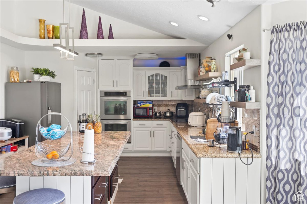 Kitchen with decorative backsplash, appliances with stainless steel finishes, vaulted ceiling, ventilation hood, and dark wood-type flooring