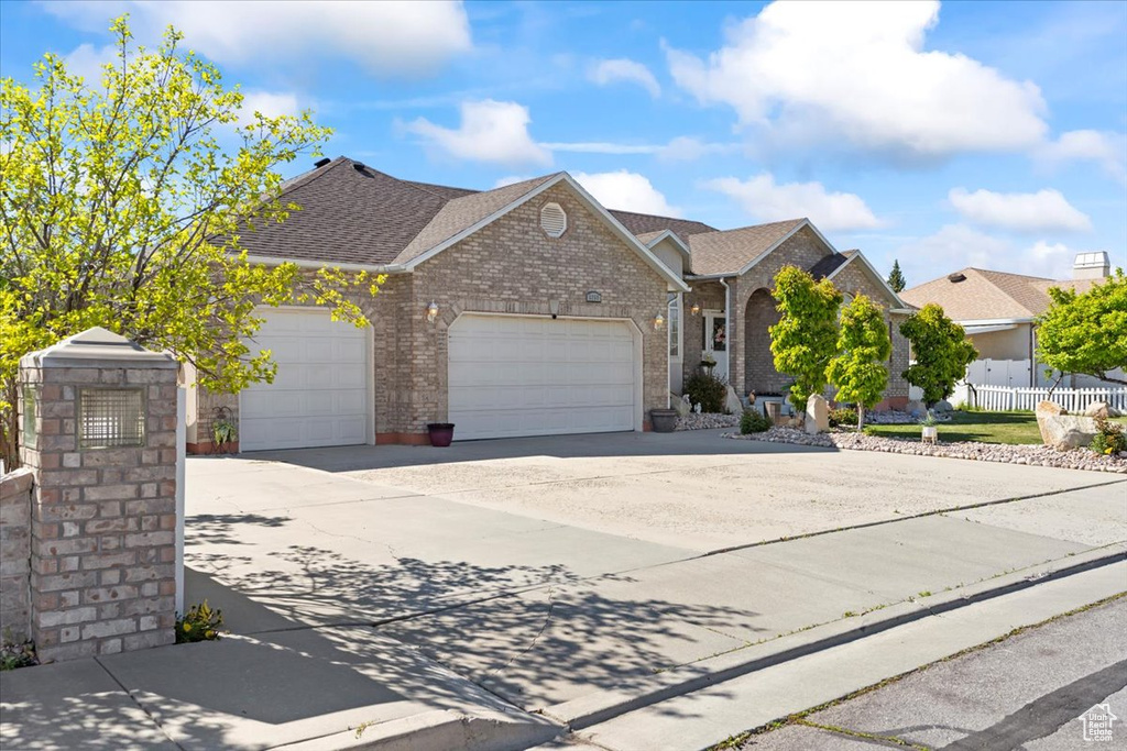 Ranch-style house featuring fence, a shingled roof, brick siding, a garage, and driveway