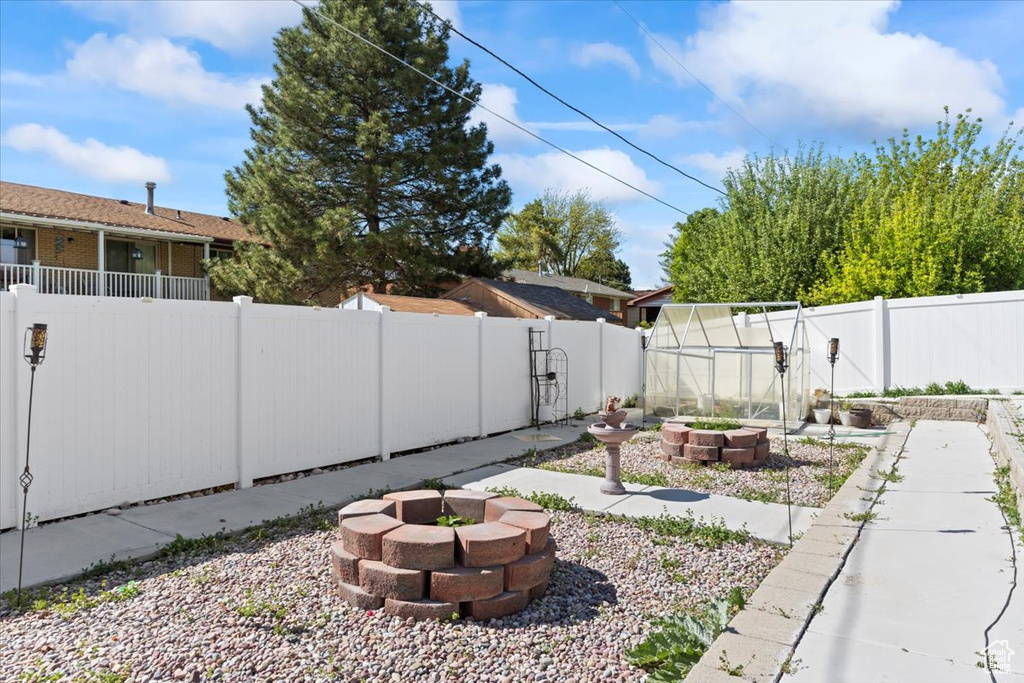 View of yard featuring a fenced backyard, a garden, a greenhouse, and an outdoor fire pit