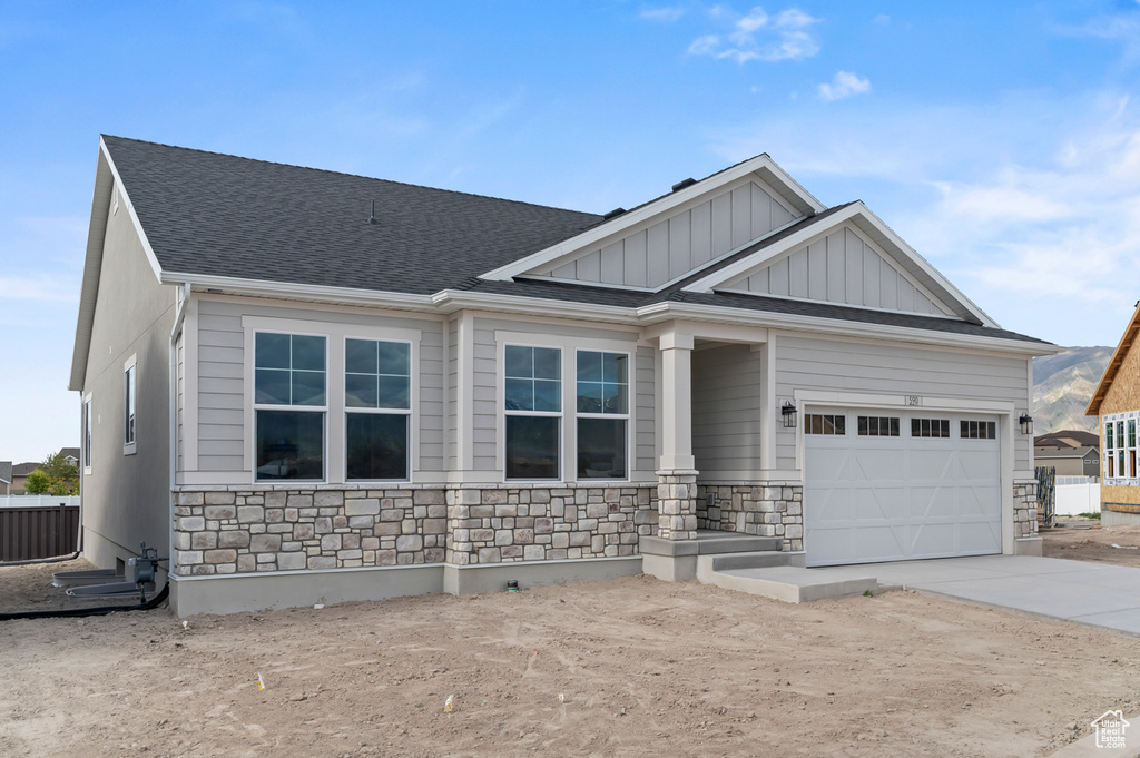 Craftsman-style home with stone siding, driveway, board and batten siding, a garage, and roof with shingles