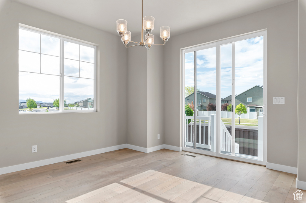 Spare room with plenty of natural light, a chandelier, baseboards, and light wood-type flooring
