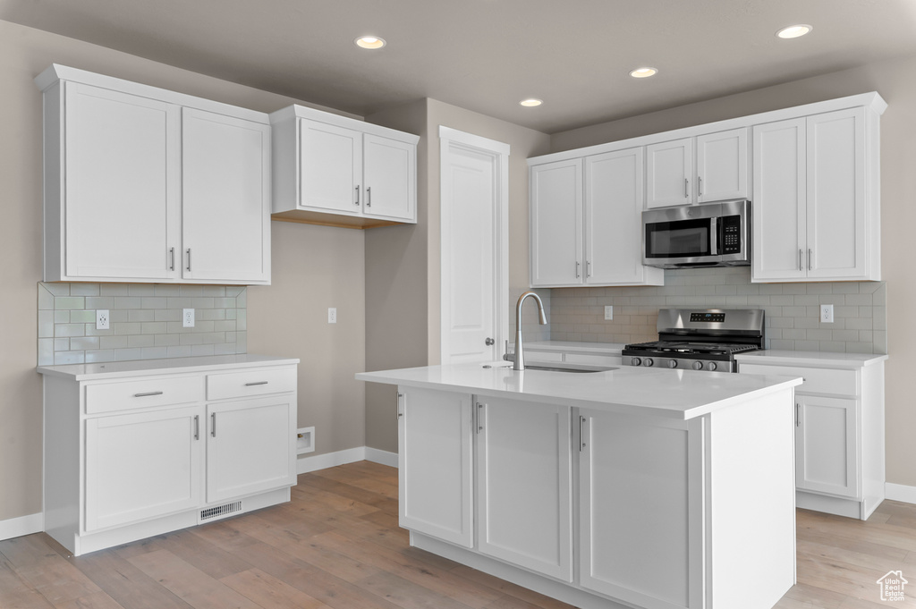 Kitchen with stainless steel appliances, a sink, baseboards, light wood-type flooring, and white cabinets