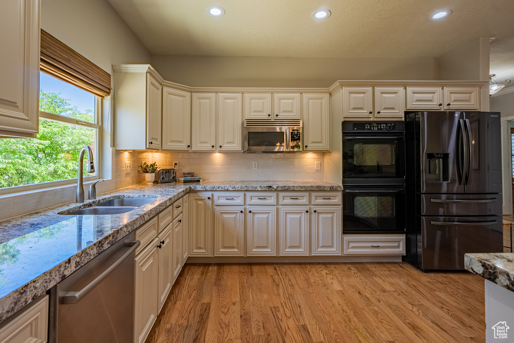 Kitchen with appliances with stainless steel finishes, recessed lighting, light wood finished floors, light stone countertops, and decorative backsplash