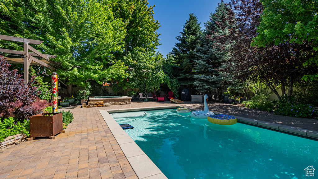 Outdoor pool featuring a patio area, an outdoor hot tub, and view of scattered trees