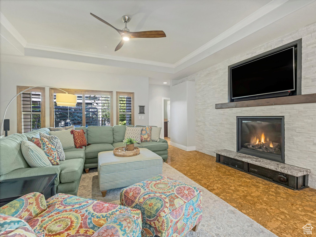 Living area featuring a ceiling fan, a stone fireplace, crown molding, baseboards, and a tray ceiling