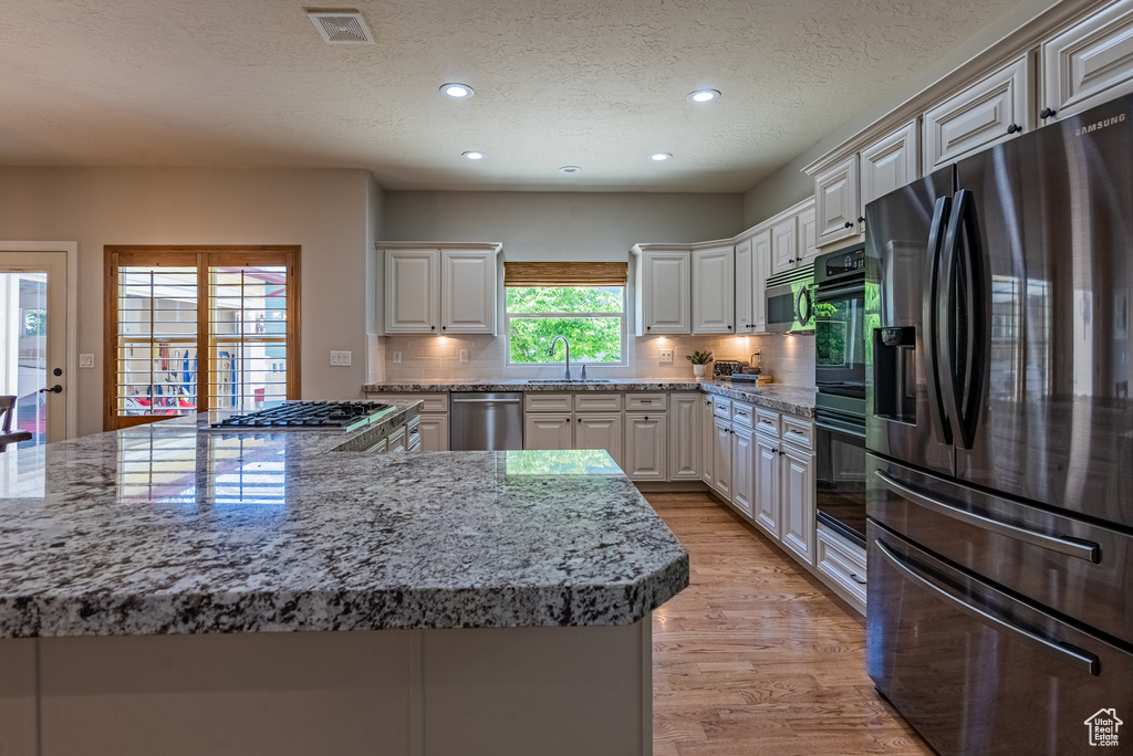 Kitchen featuring appliances with stainless steel finishes, recessed lighting, light wood finished floors, backsplash, and white cabinets