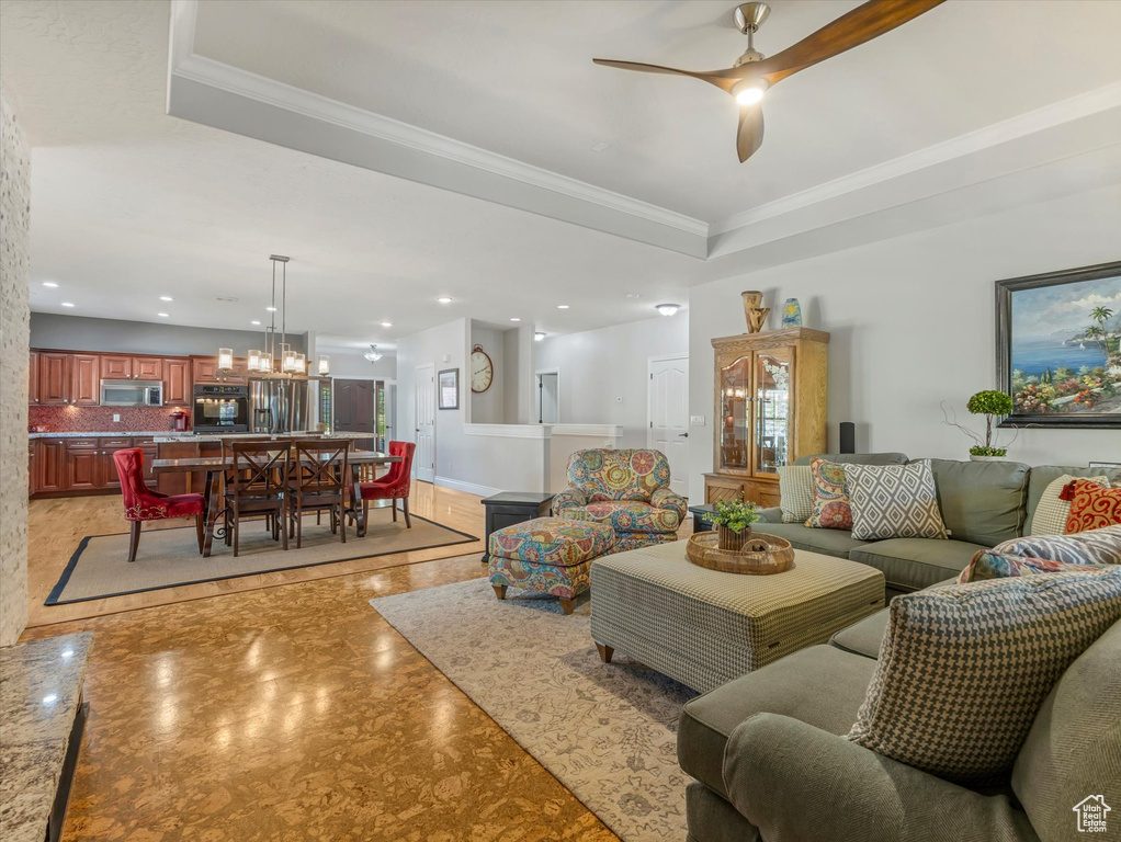 Living area featuring a raised ceiling, recessed lighting, ornamental molding, and ceiling fan with notable chandelier